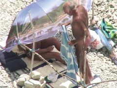 Зрелые нудисты занимаются сексом под зонтом на пляже